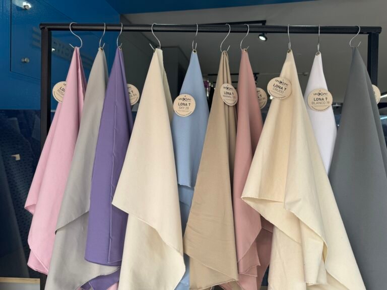 Telas colgadas en el taller: rosados, lilas, beige y grises